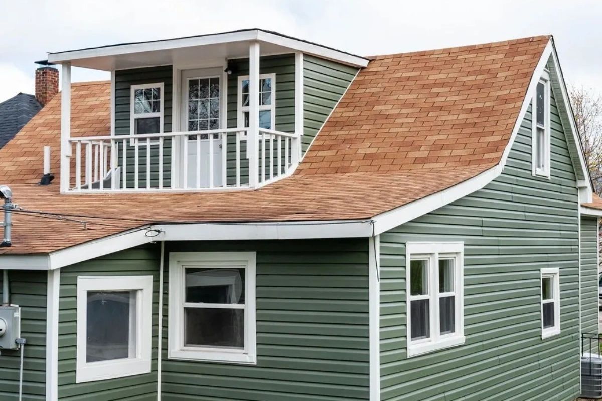 A green house with a brown roof and a balcony.