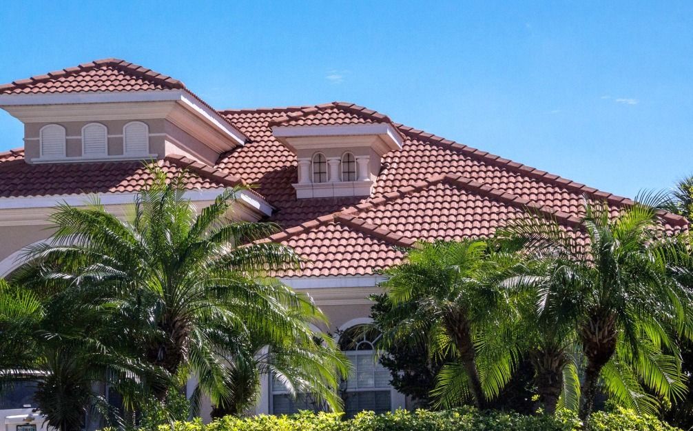 A large house with a tiled roof and palm trees in front of it.