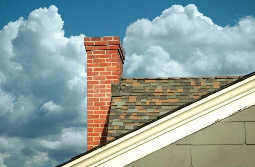 A brick chimney on top of a roof with clouds in the background