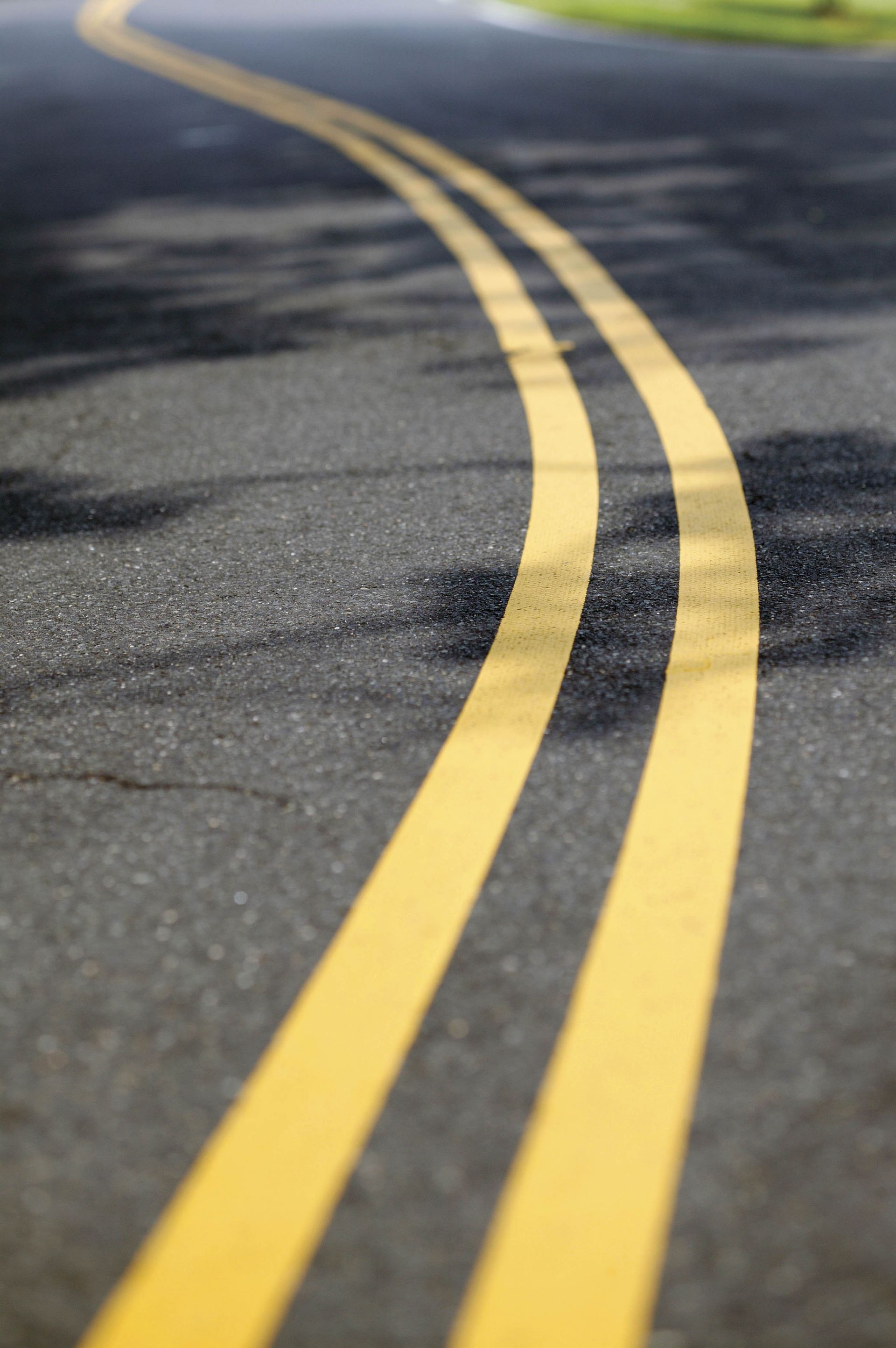 Yellow double lines on a curving asphalt road, with blurred background and shadows.