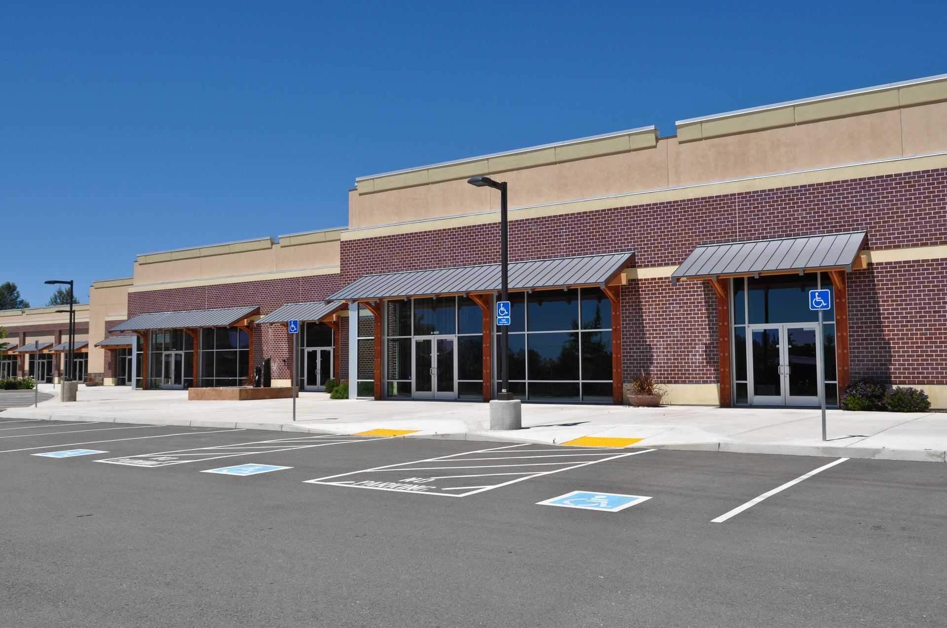 Strip mall with storefronts, awnings, and accessible parking spaces, blue sky.