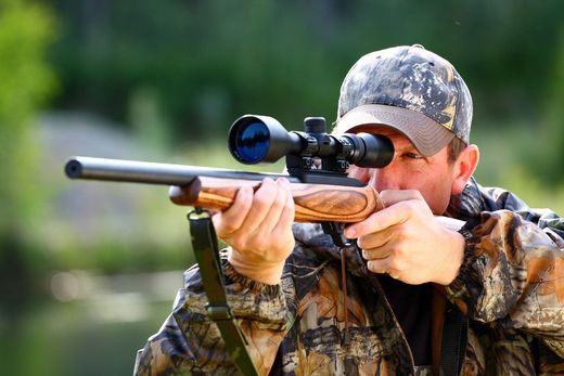 Male hunter aiming through scope of rifle