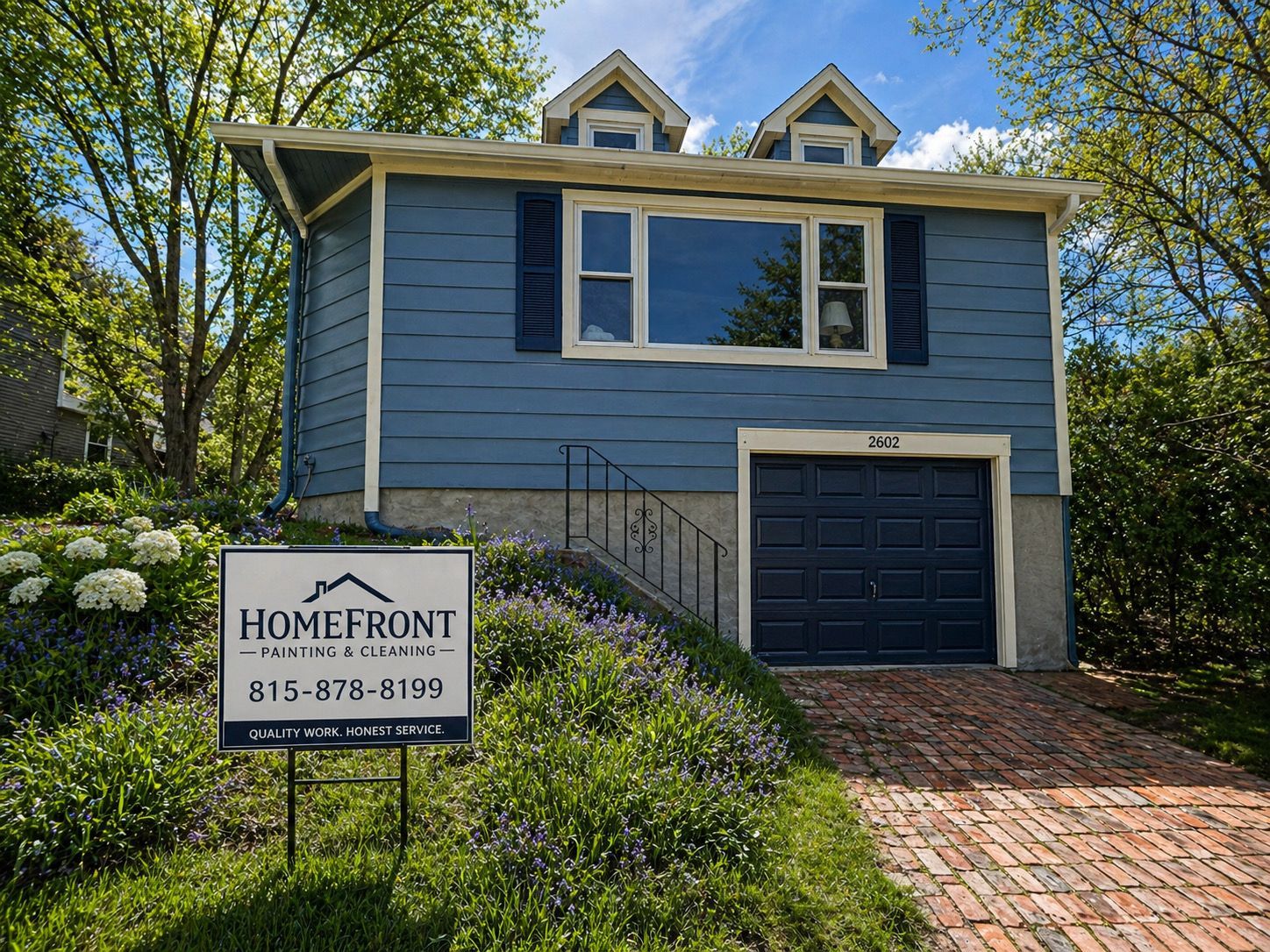 Blue house with a garage and brick driveway, with a Homefront Realty sign in the front yard.