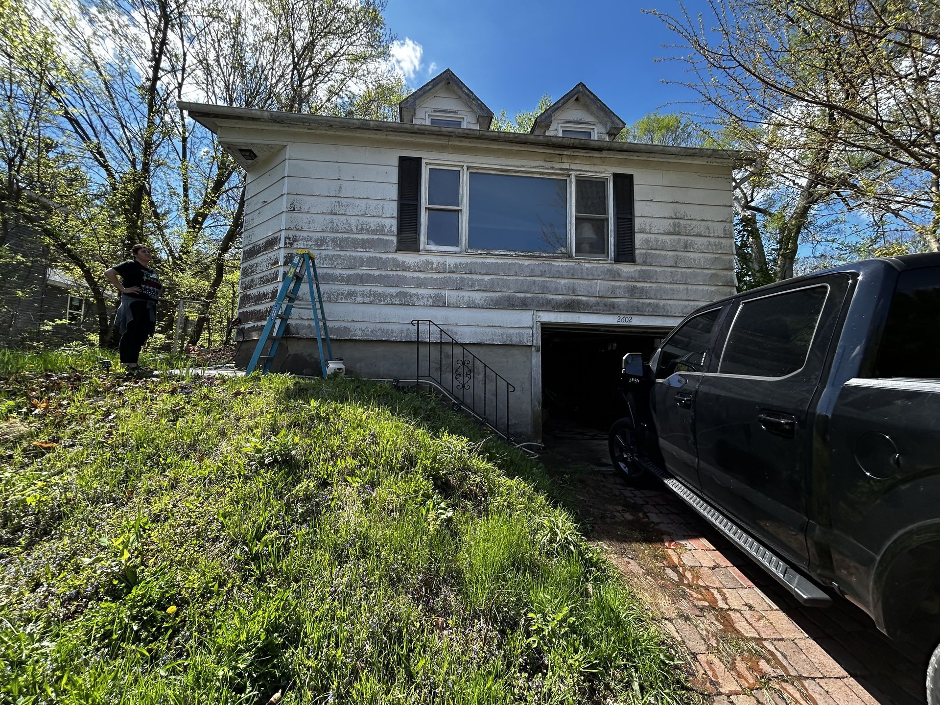 Weathered white house on a hill with a black truck parked beside the driveway.