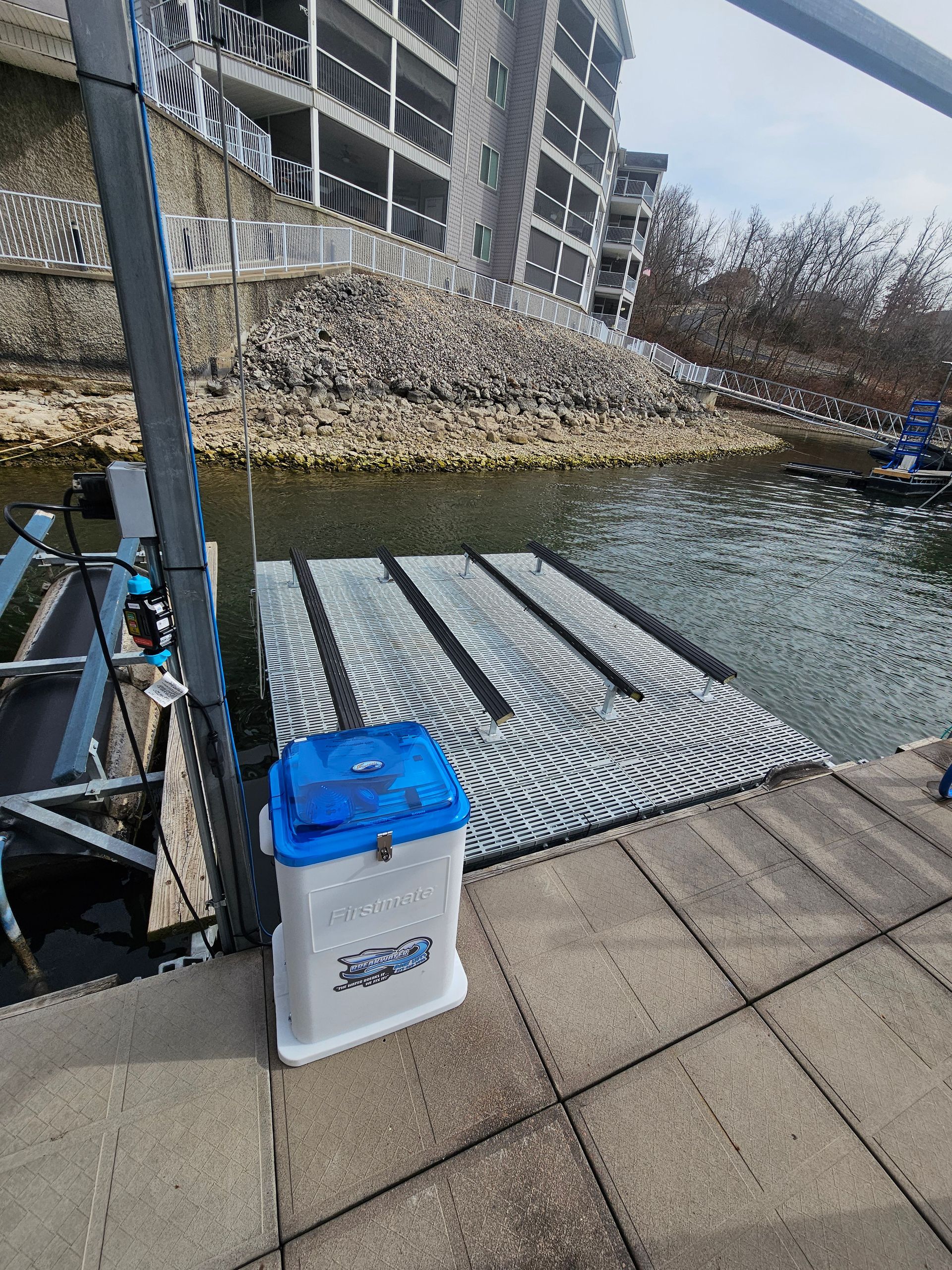 A blue cooler is sitting on a dock next to a body of water.