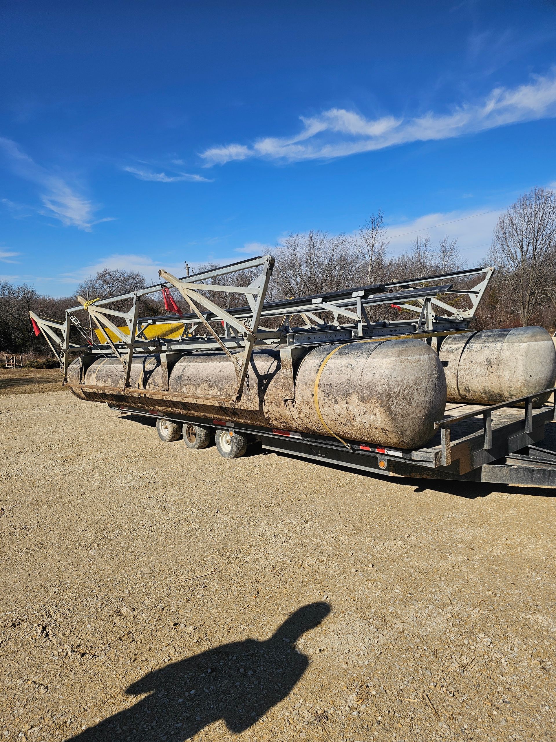 A row of pontoon boats are sitting on top of a trailer in a gravel lot.