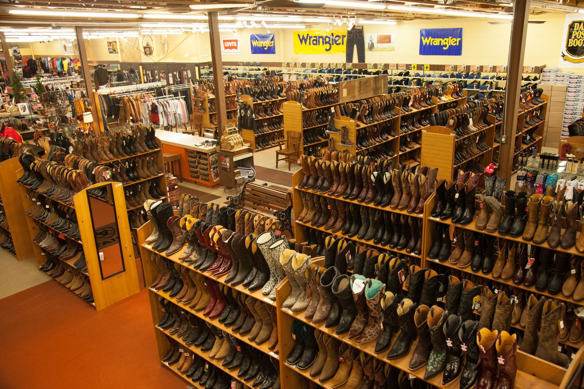 A large retail store aisle filled with numerous rows of shelves stocked with various styles of leather cowboy boots.