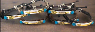 Four braided leather bracelets with gold arrow-shaped metal plates and turquoise accents, arranged on a wooden surface.