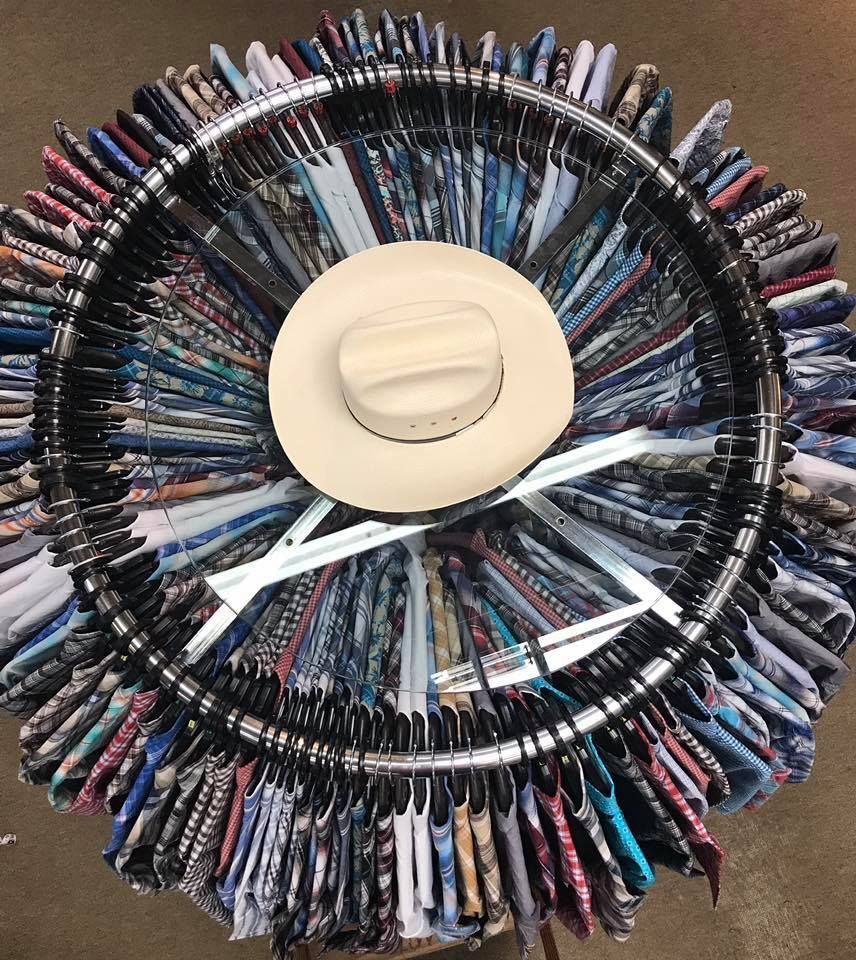 A top-down view of a circular rack densely packed with hanging patterned shirts, with a single light-colored cowboy hat.