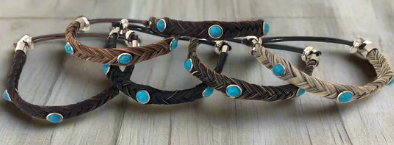 Four braided bracelets in varying shades of brown, each decorated with inlaid turquoise stones, set on a wooden surface.