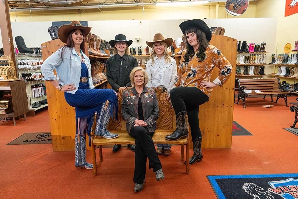 Five people wearing cowboy hats pose in a retail store filled with boots and western apparel.