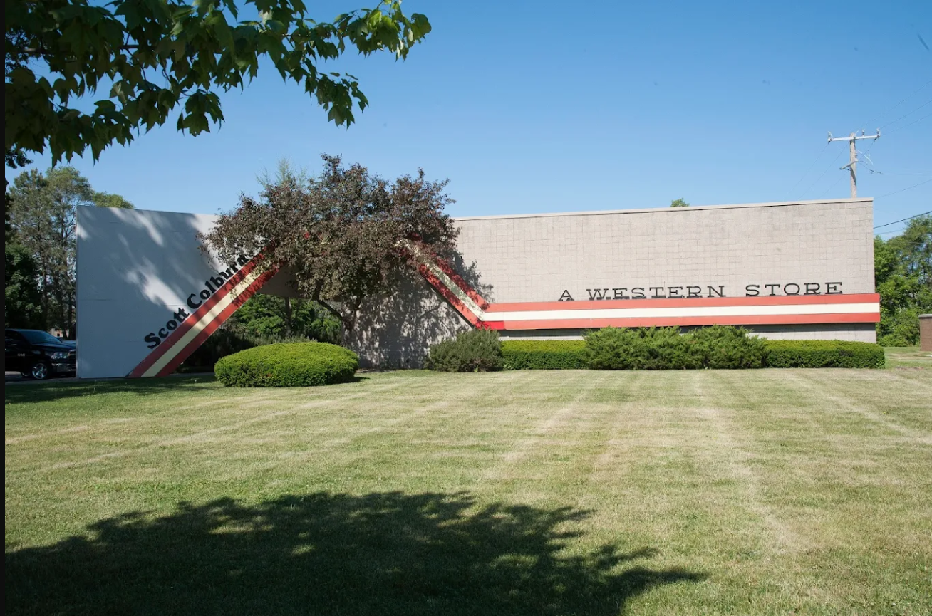 A neutral-colored building wall features a stylized, diagonal brown and orange stripe, with text reading 