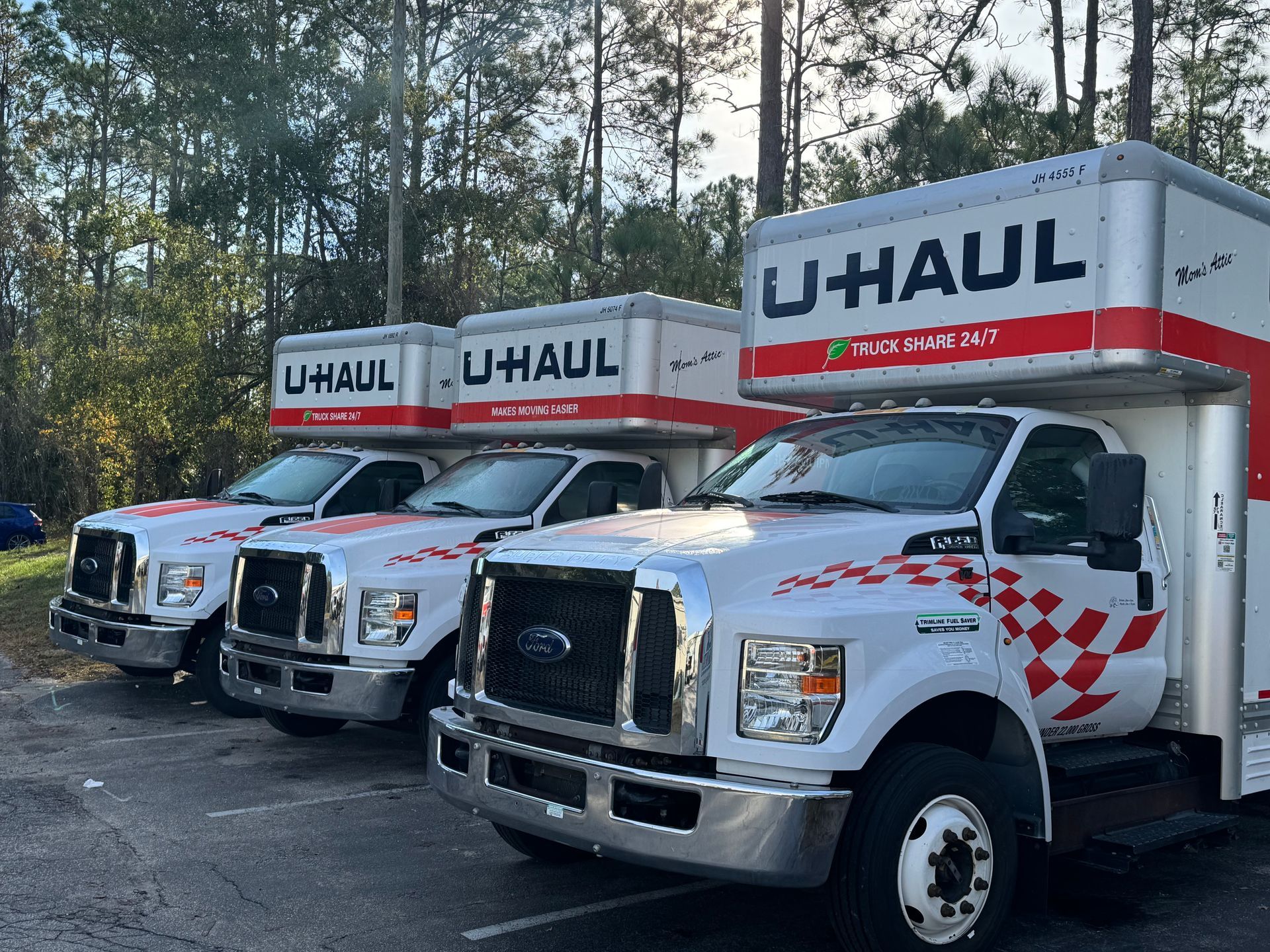 Three U-Haul moving trucks parked in a row outdoors among trees