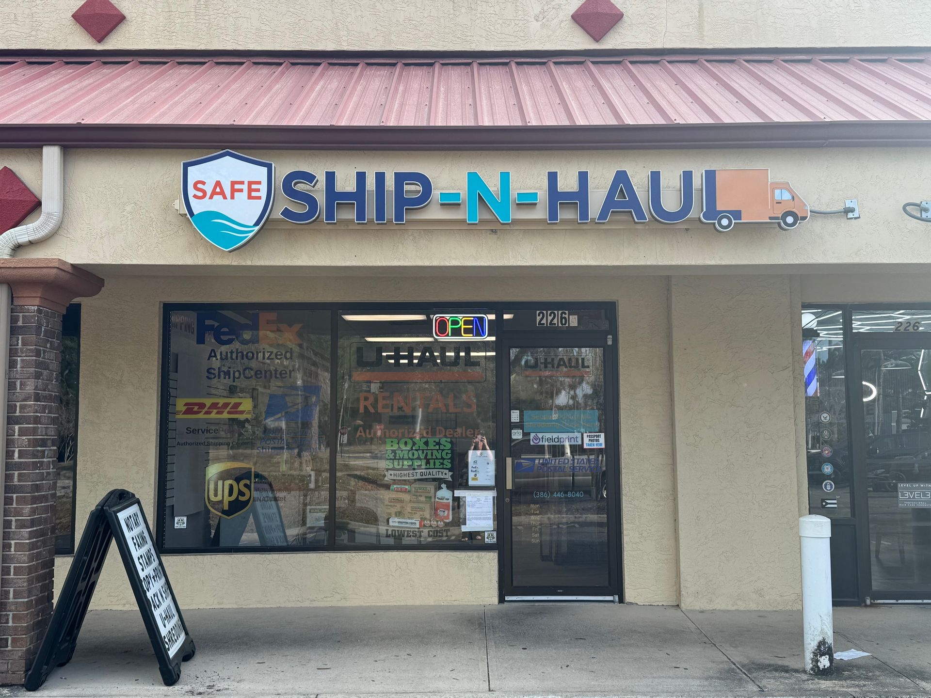 Storefront of Safe Ship-N-Haul with beige facade and a glass door, featuring a black A-frame sign outside.
