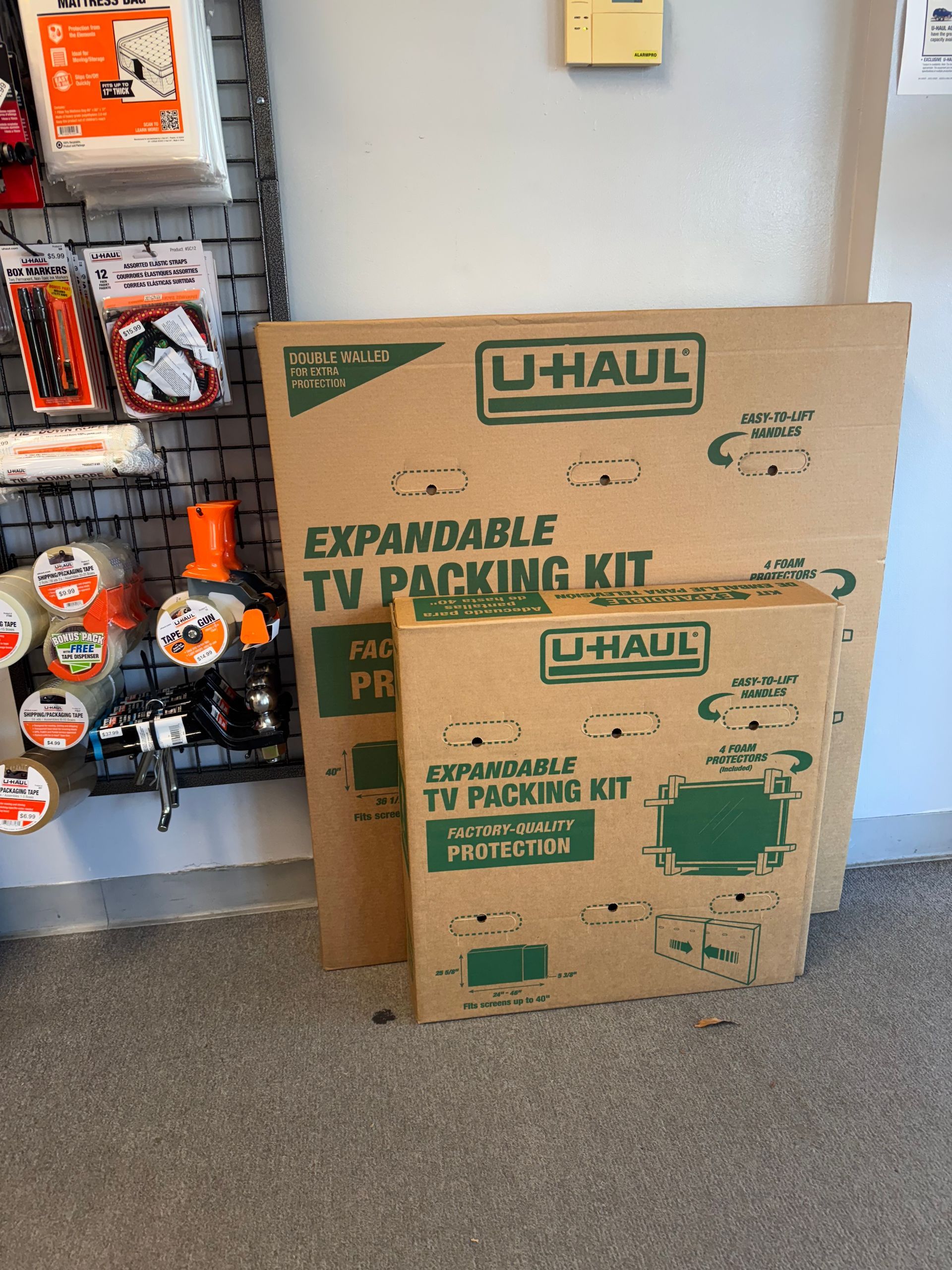 U-Haul expandable TV packing kit boxes in a store aisle beside hanging packing supplies