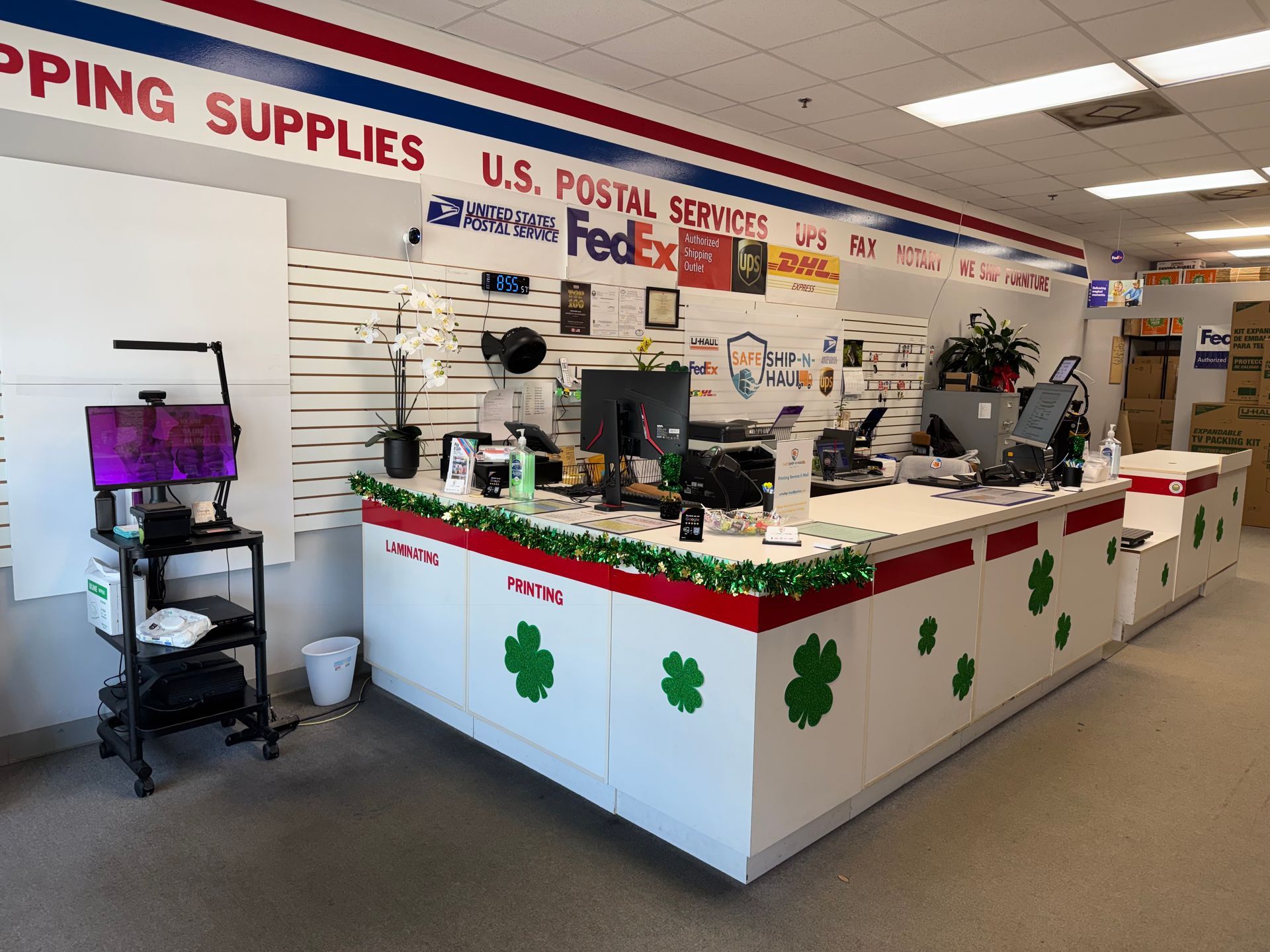 Shipping counter with USPS and FedEx signs, decorated with green clovers and gift baskets inside a store