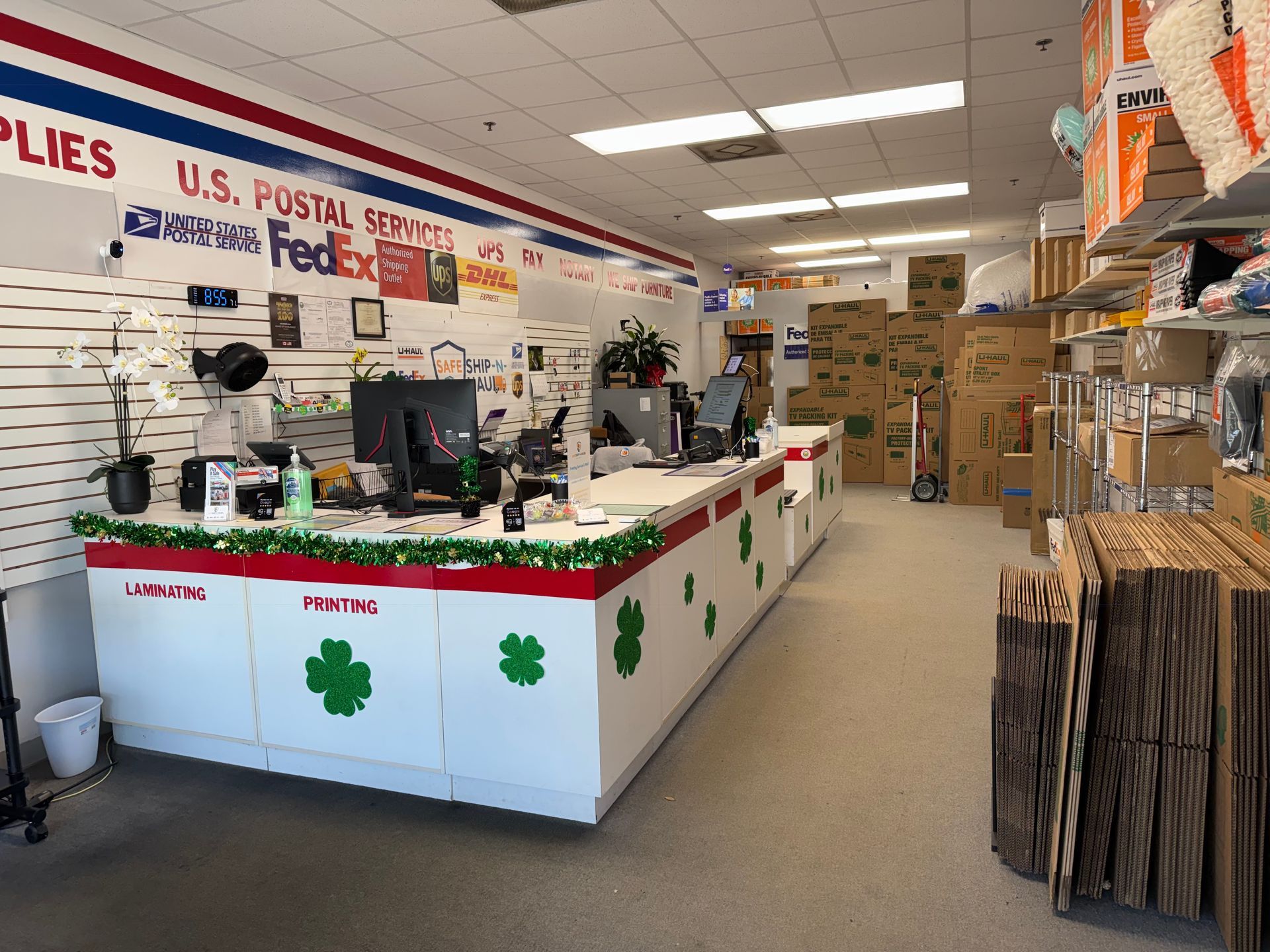 Postal service counter inside a store, with U.S. Postal Service signs, boxes, and shipping supplies.
