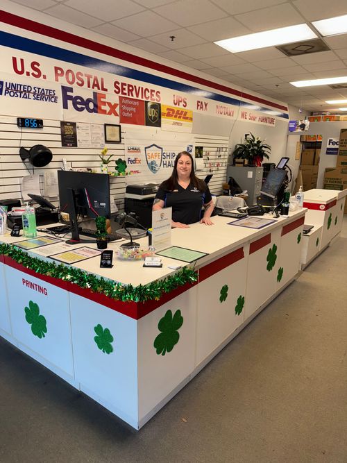 Postal counter in a U.S. Postal Service office, decorated with shamrocks, with a woman standing behind it.