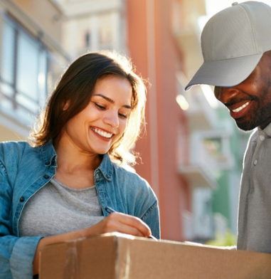 Two smiling people loading a cardboard box outdoors