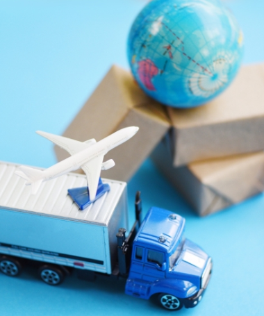 Blue toy truck carrying a white airplane beside a globe and stacked boxes