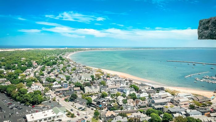 Aerial view of a coastal town with turquoise water, sandy beach, and dense greenery under a bright blue sky