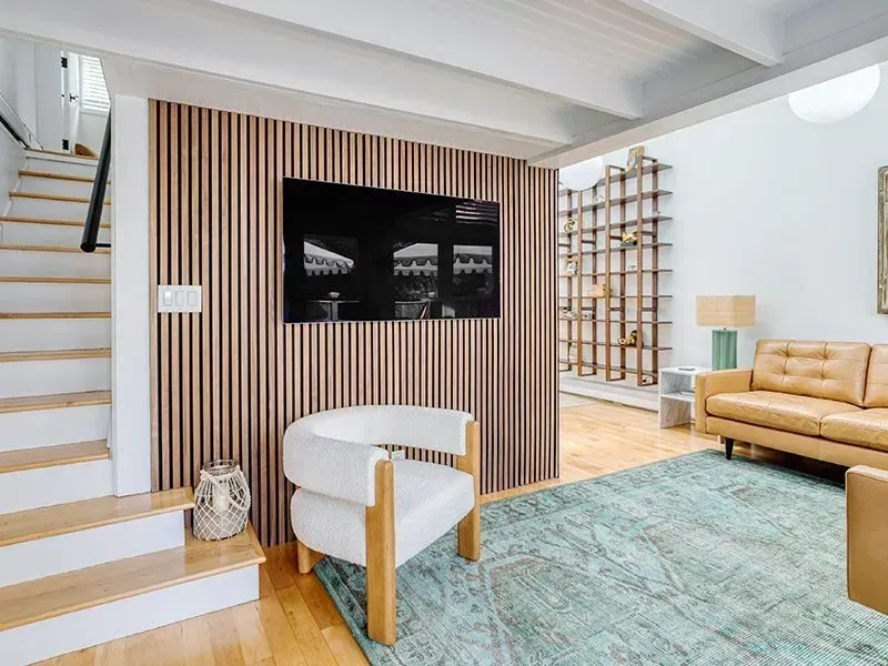 Bright modern living room with striped wood wall, white chair, tan sofa, and blue rug