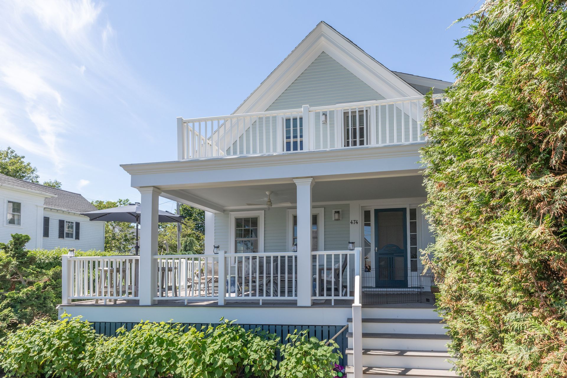 Gray beach house with white railings, front porch, and balcony in bright sunlight
