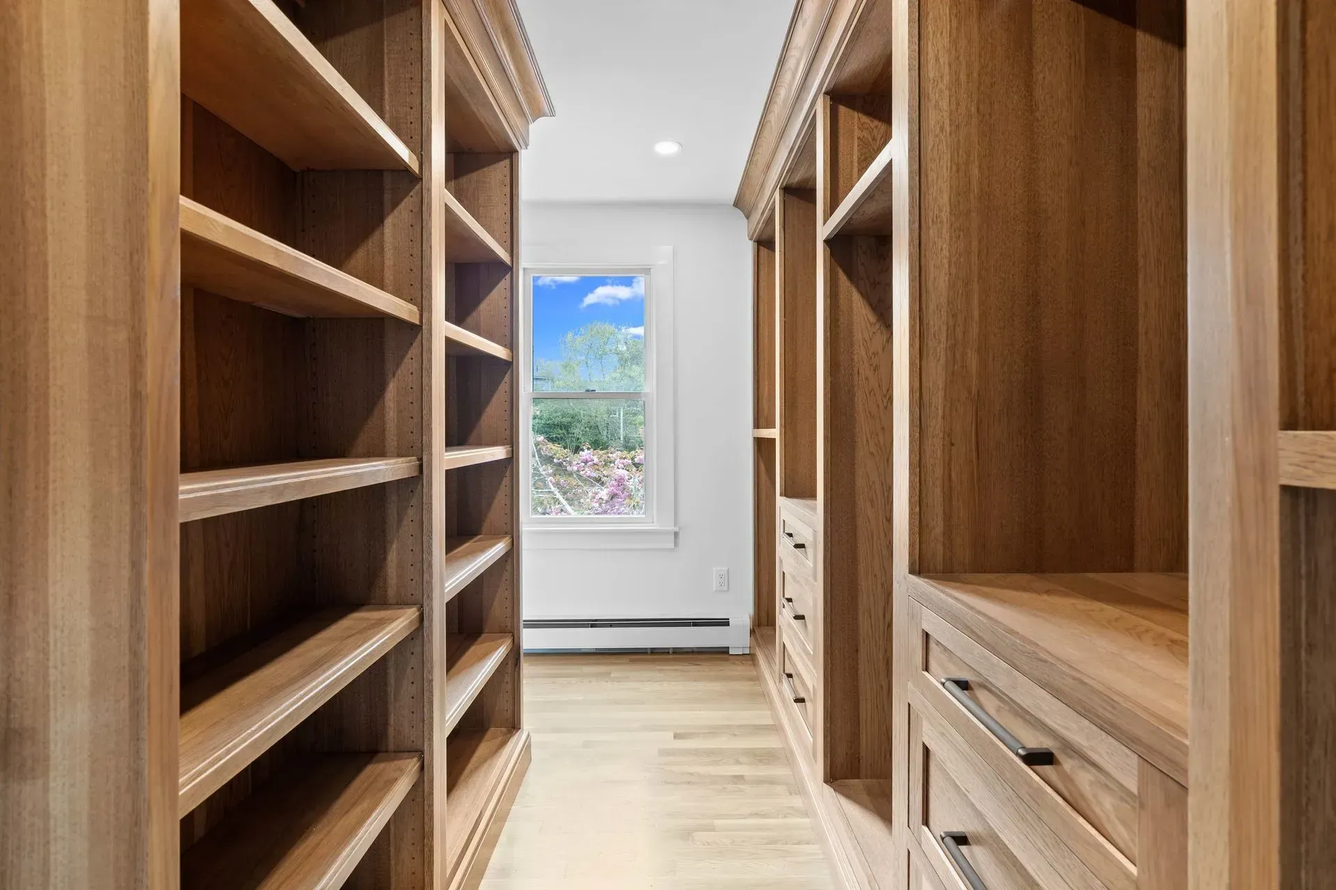 Walk-in closet with built-in wooden shelves and drawers, viewed toward a window with a mountain view.