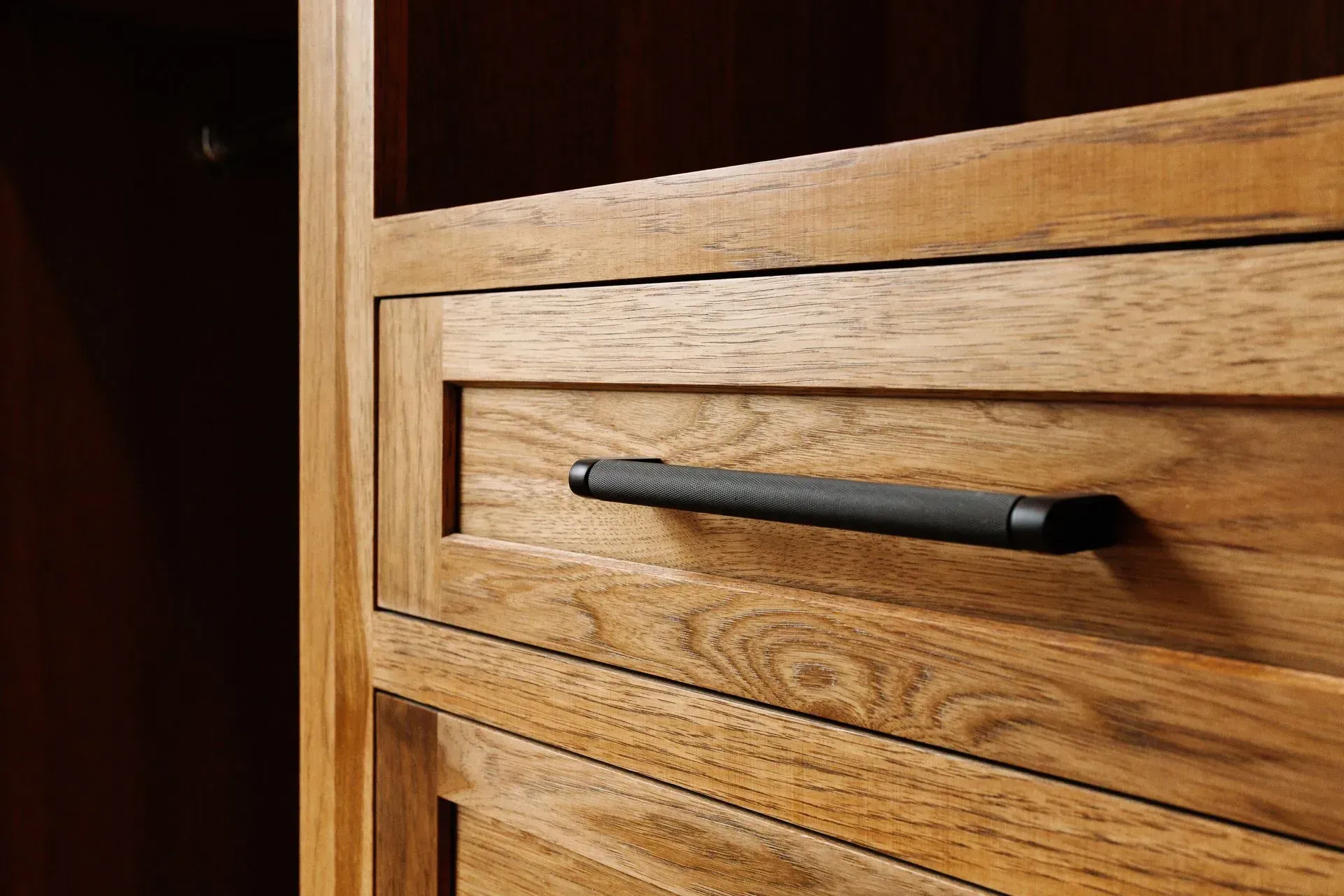 Close-up of a wooden drawer with a black handle in warm indoor light