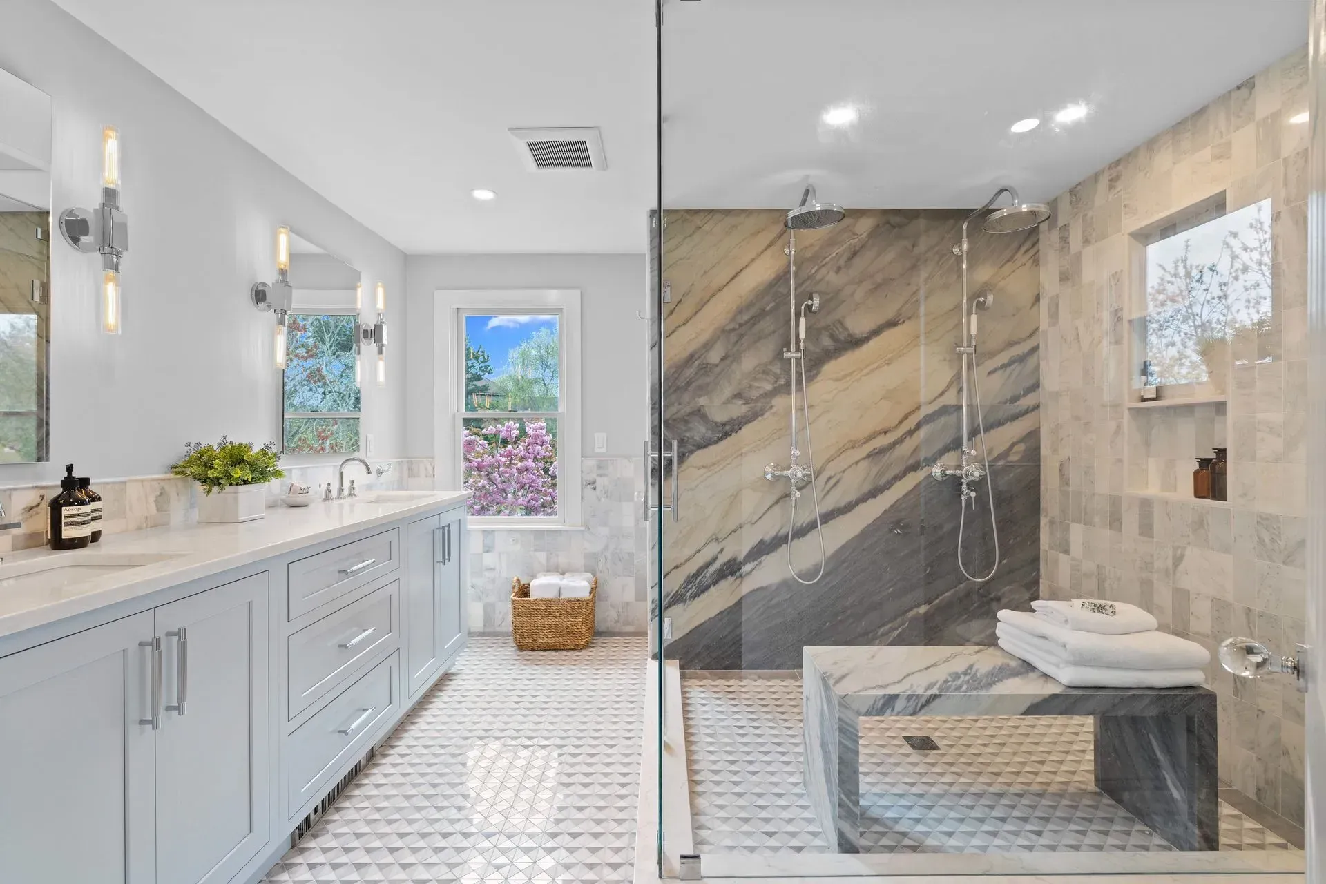 Bright modern bathroom with white vanity, marble shower wall, and bench near a window.