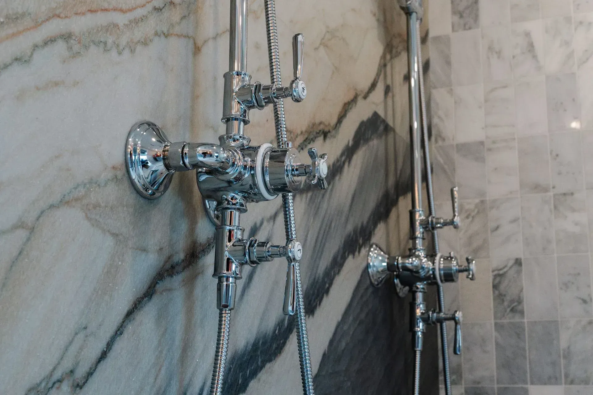 Chrome shower fixture mounted on a marble-tiled bathroom wall