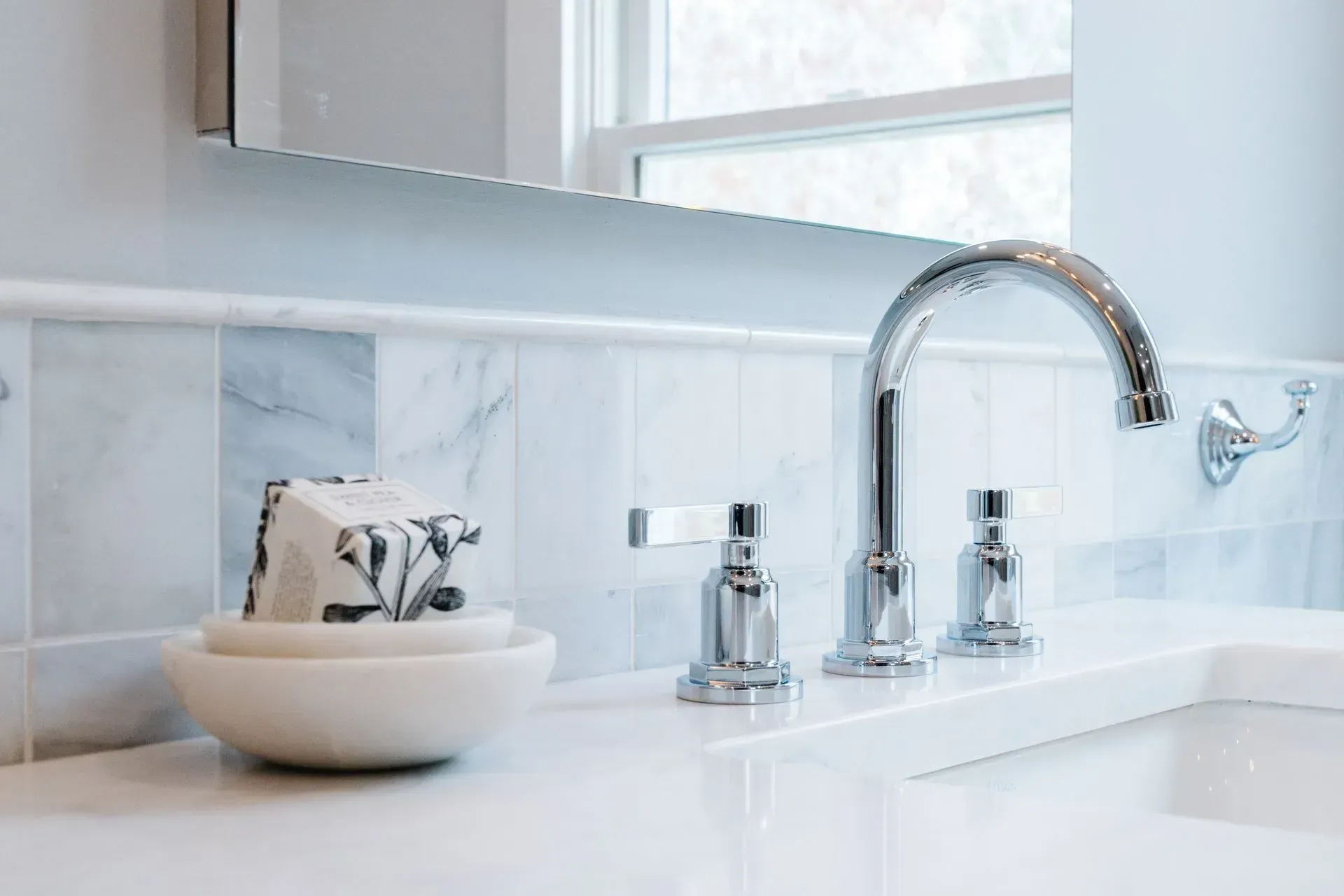 Bright bathroom sink with chrome faucet, marble tile backsplash, soap dispenser, and bowl with hand towels.