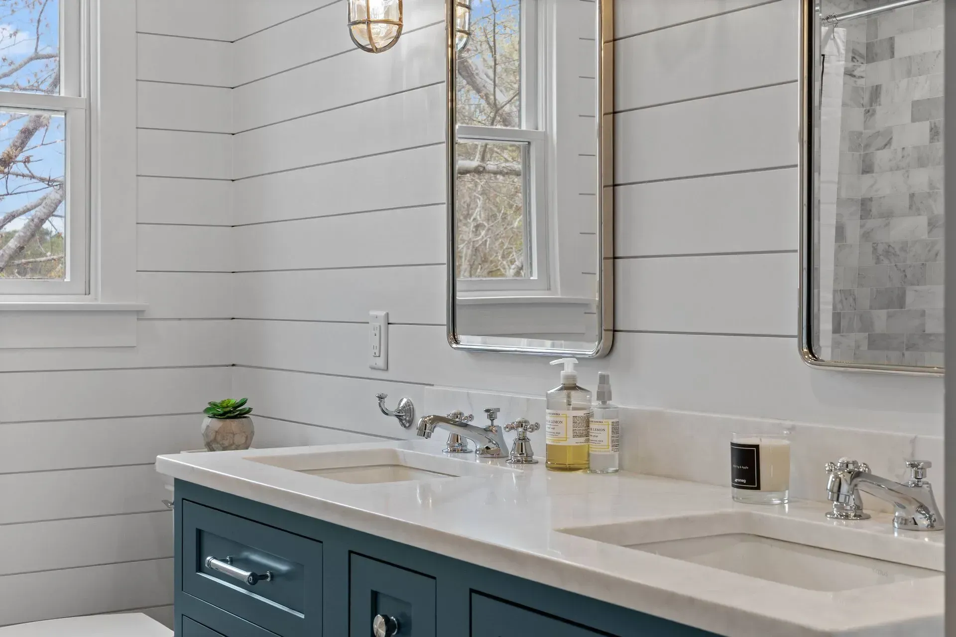 Modern bathroom vanity with blue cabinets, white countertop, mirrors, and chrome faucets by a window.