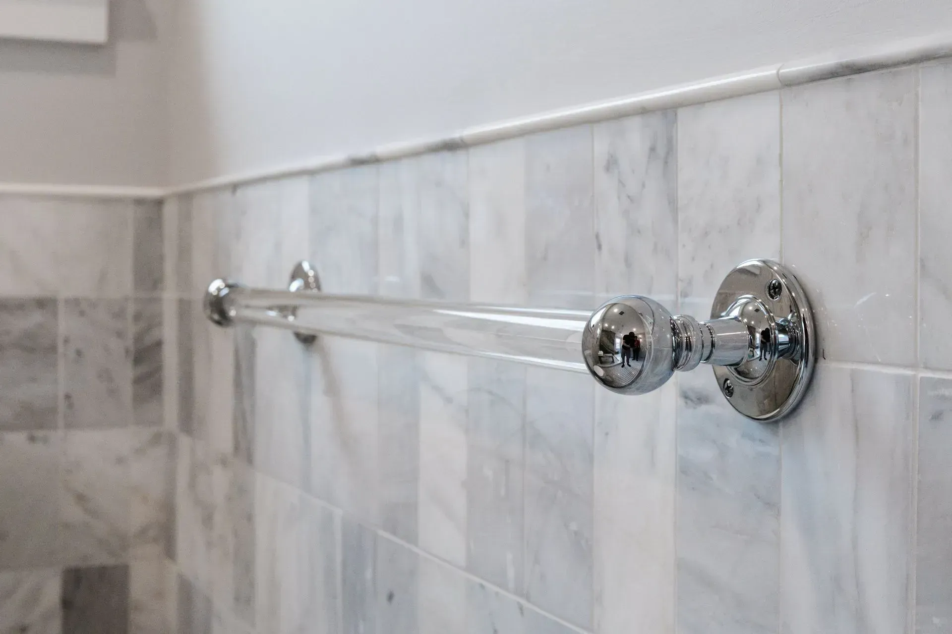 Chrome towel bar mounted on a white marble-tiled bathroom wall
