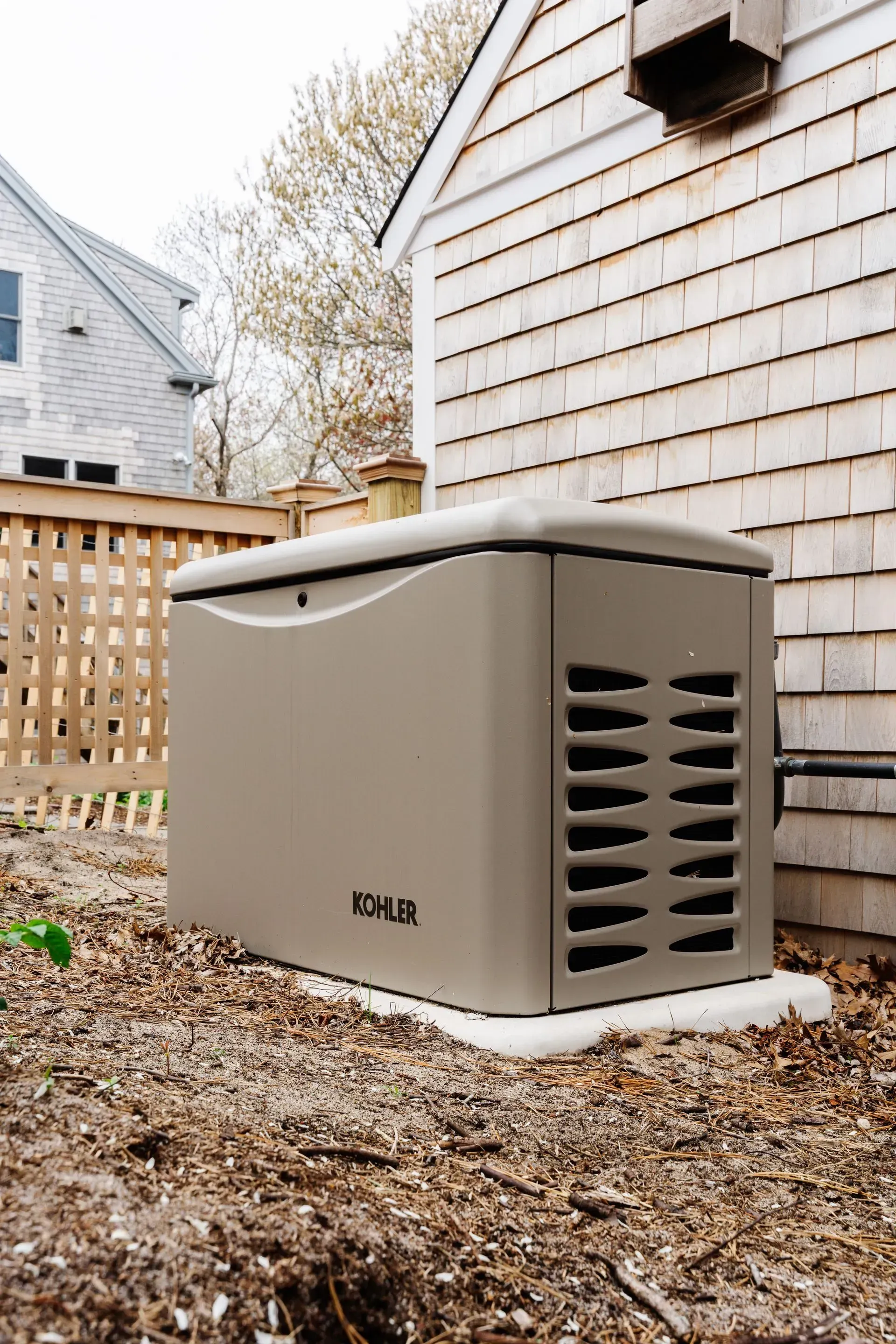 Outdoor beige generator unit beside a house, partially covered in snow.