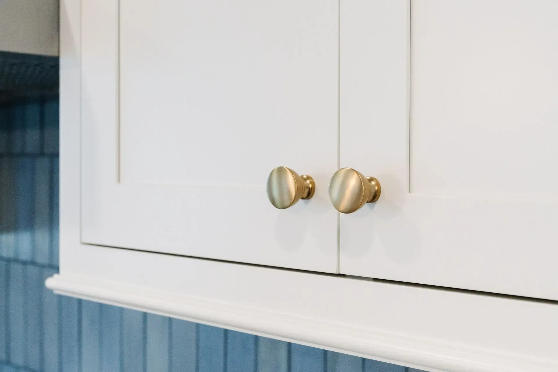White cabinet with brass knobs above blue tile backsplash