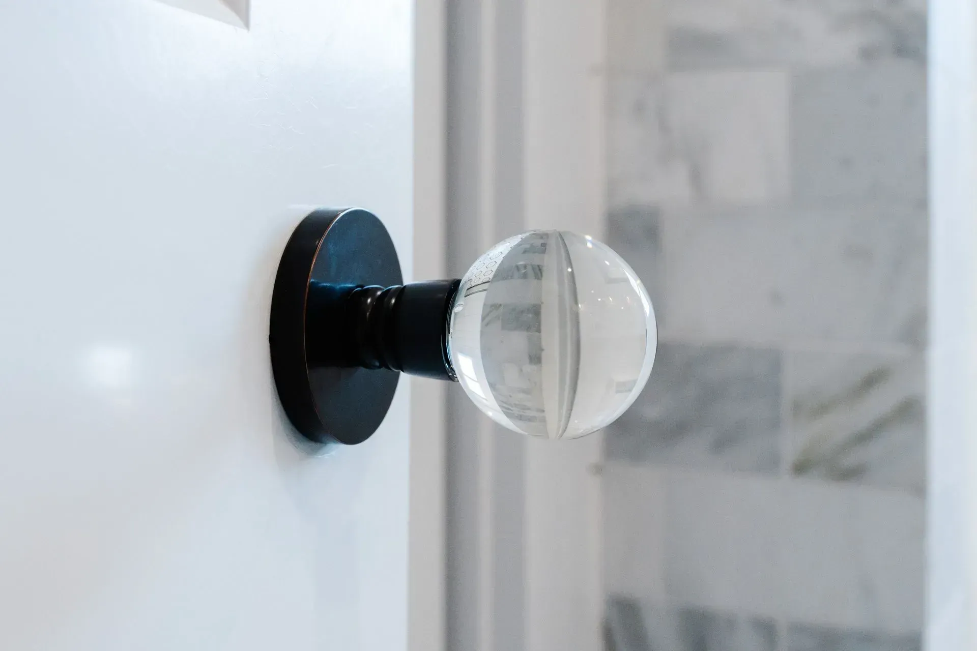 Clear glass doorknob on a white door with a black base, near a tiled bathroom wall