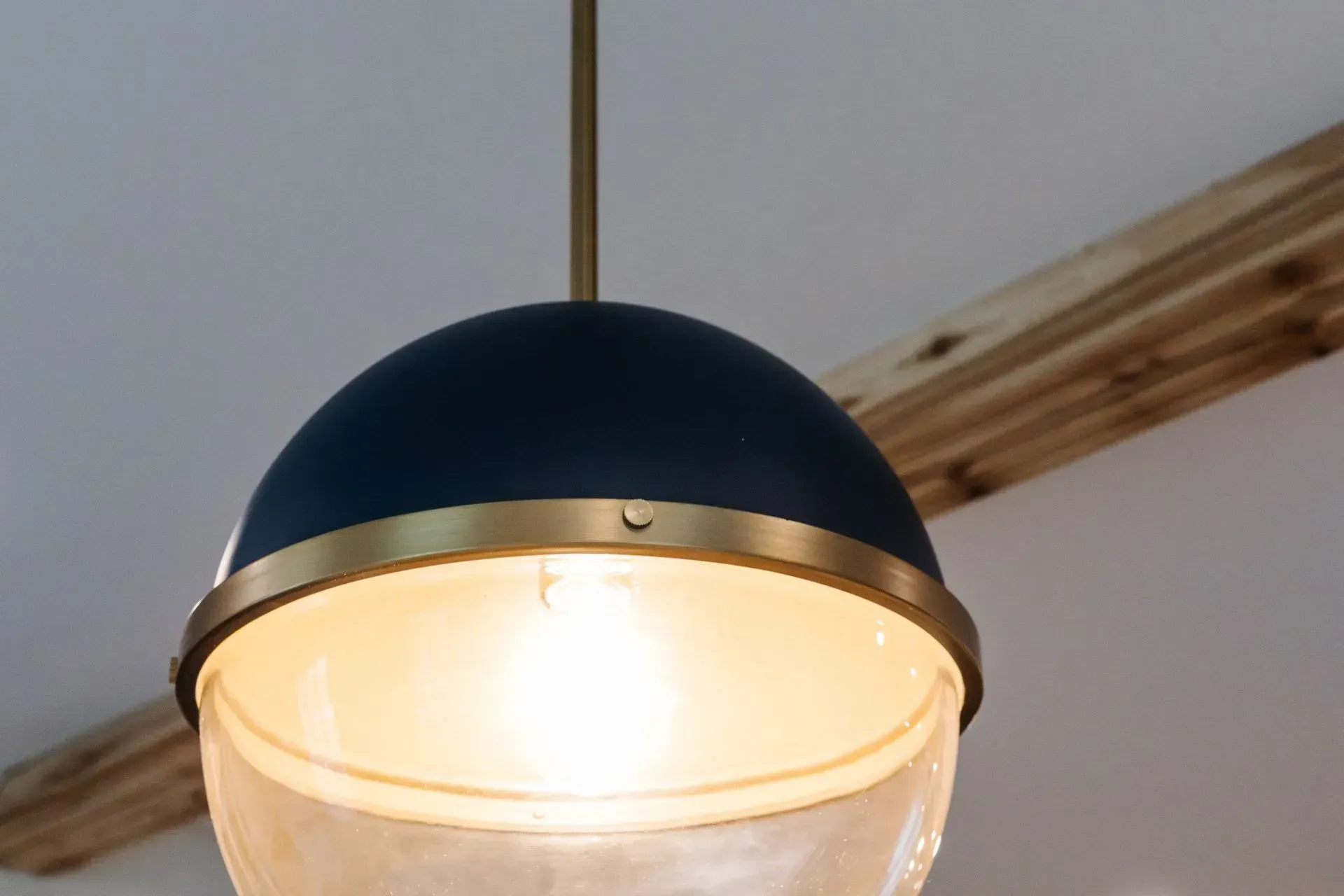 Close-up of a hanging black-and-clear glass pendant light with a warm glow