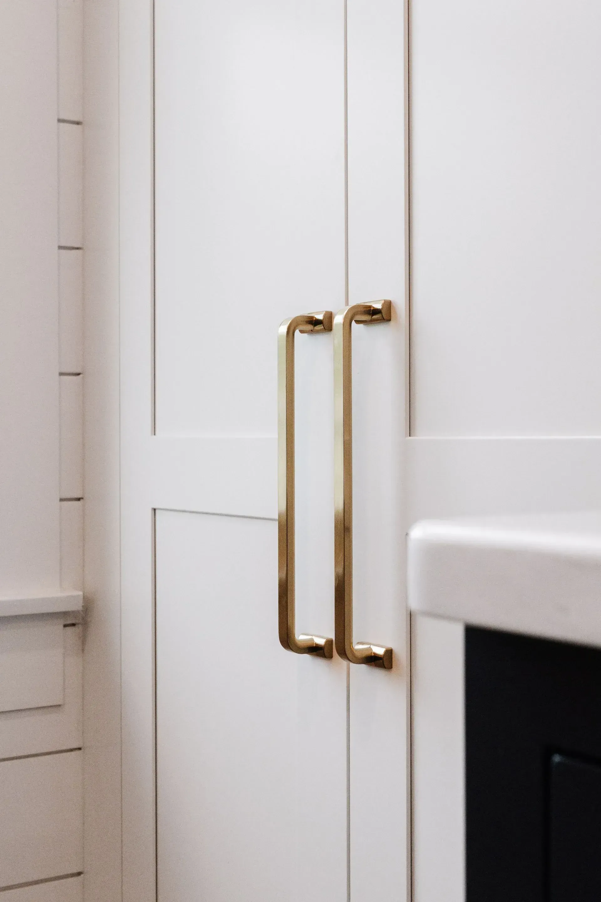 White cabinet doors with gold handles beside a white sink in a bathroom.