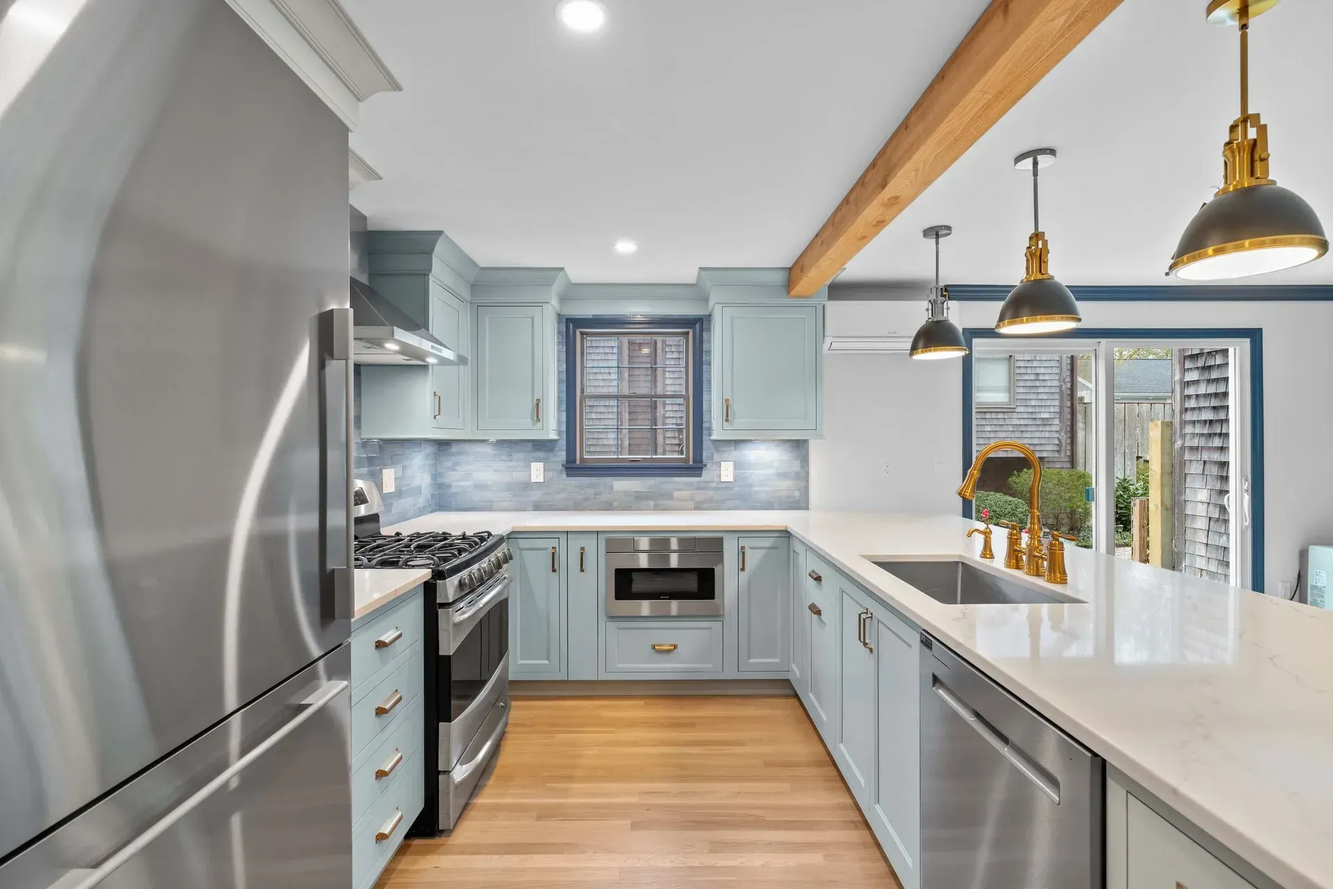 Bright modern kitchen with light blue cabinets, stainless steel appliances, white counters, and wood floors.
