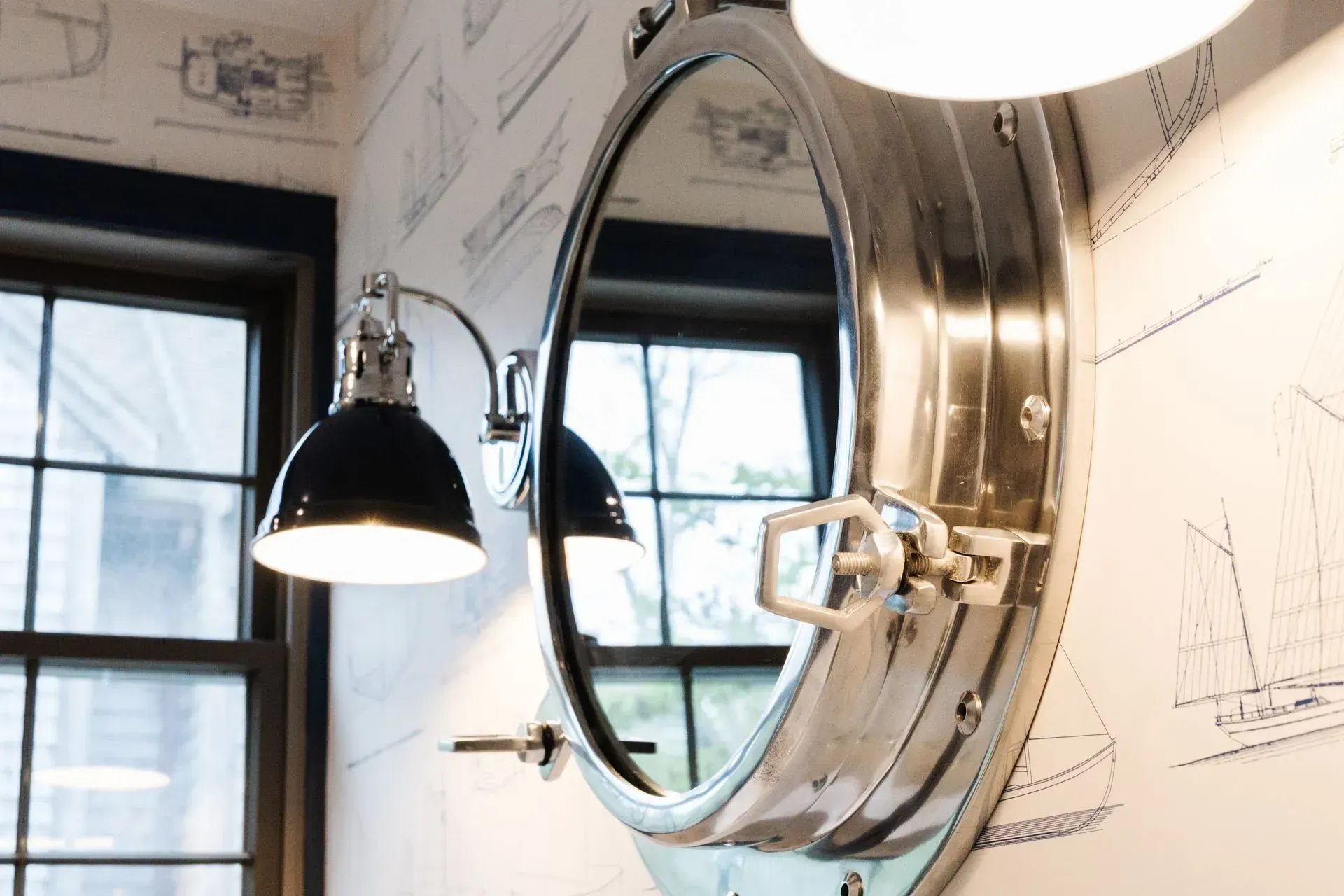Oval mirror and black wall lamp in a bright room with sketch-covered walls