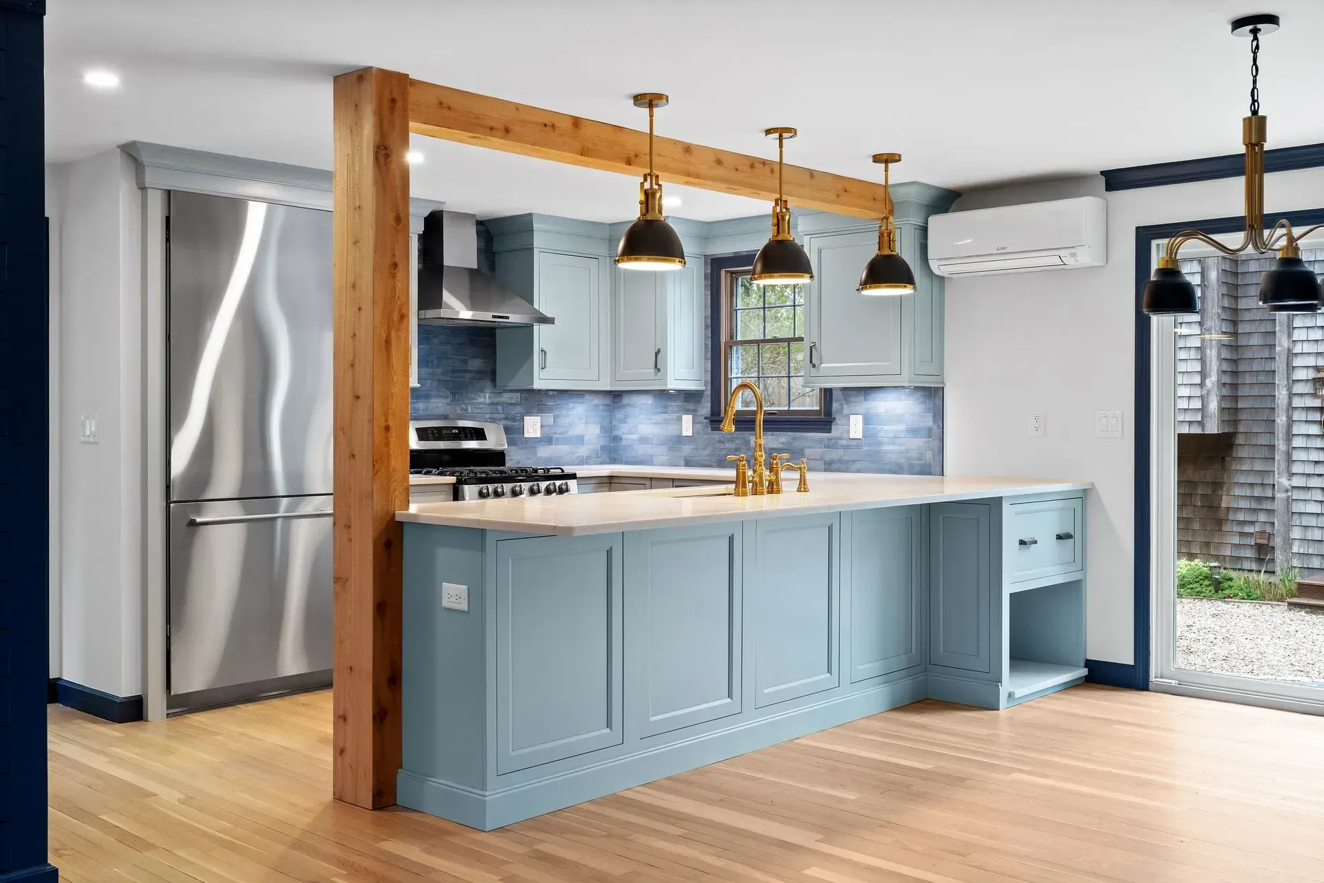 Modern kitchen with blue island, wooden beams, pendant lights, and stainless steel appliances