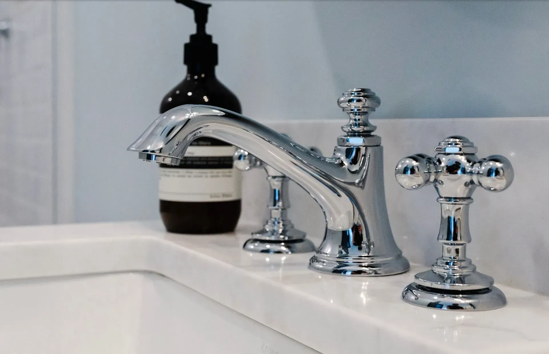 Chrome bathroom faucet on a white sink with a soap dispenser in the background