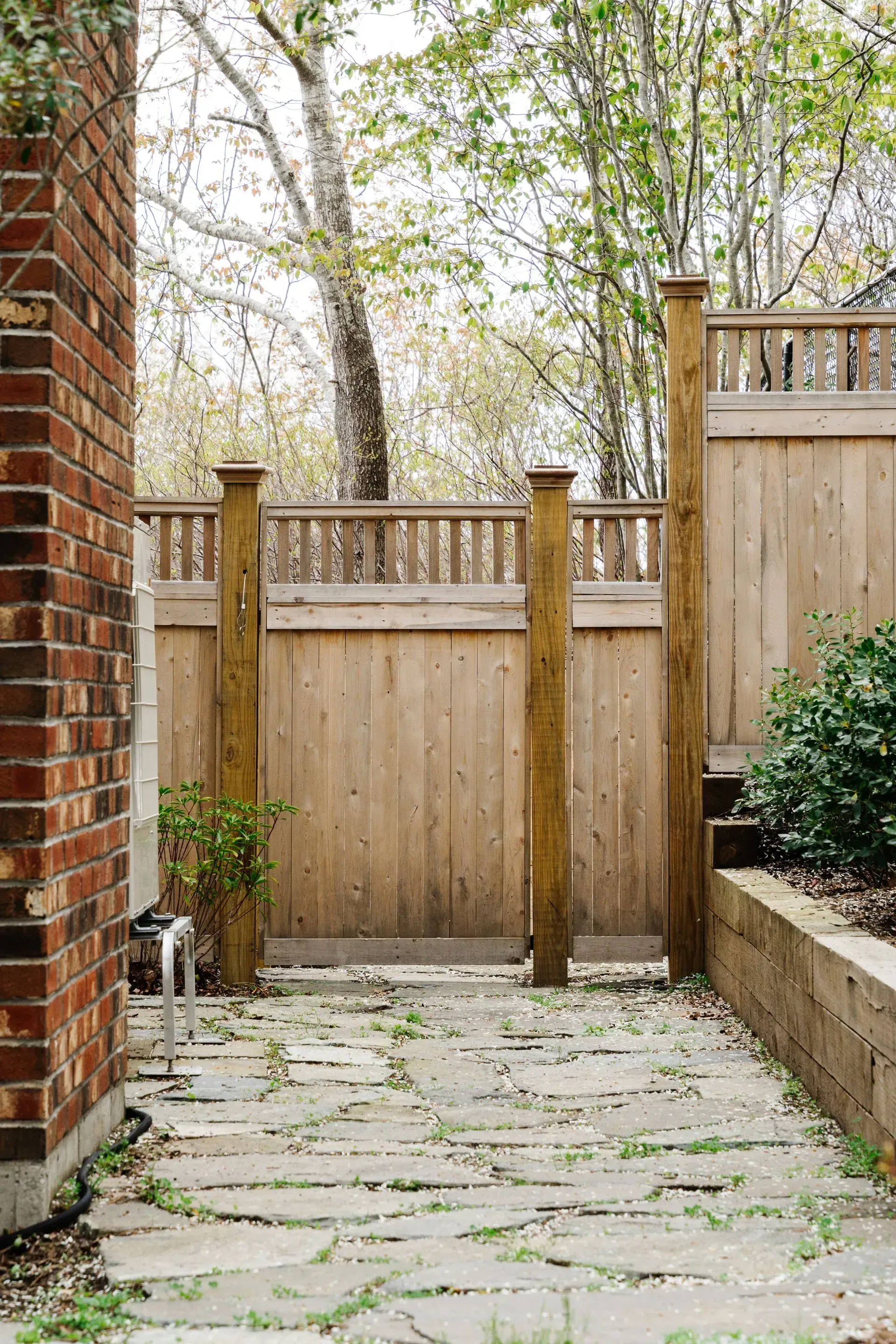 Stone patio leading to a wooden fence gate in a leafy backyard garden