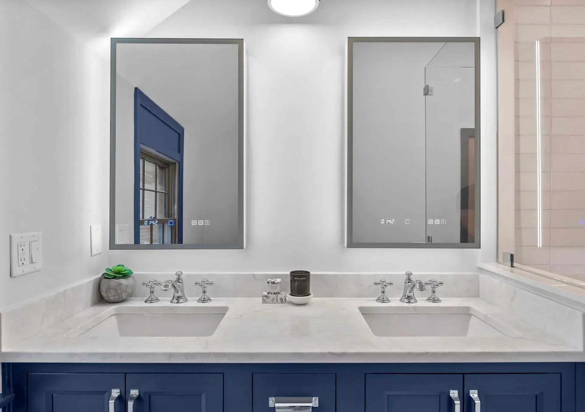 Double vanity bathroom with white counters, navy cabinets, and two mirrors above sinks