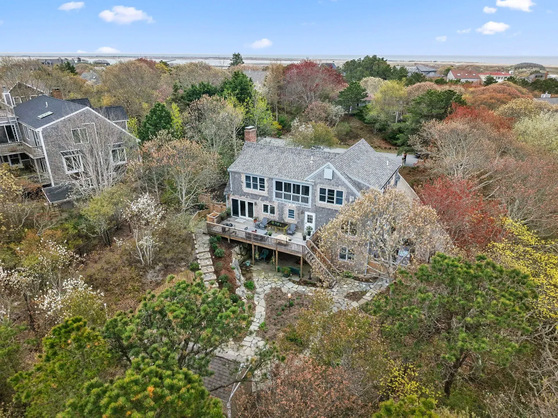 Aerial view of a gray house surrounded by dense autumn trees and neighboring homes.