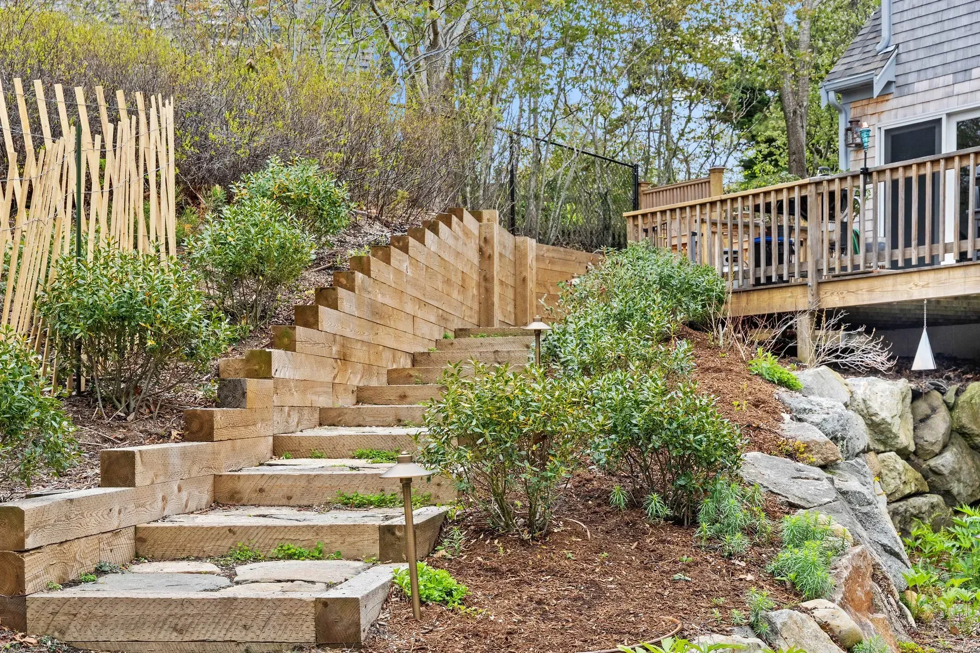 Stone steps lead up a landscaped garden beside a wooden deck and house.