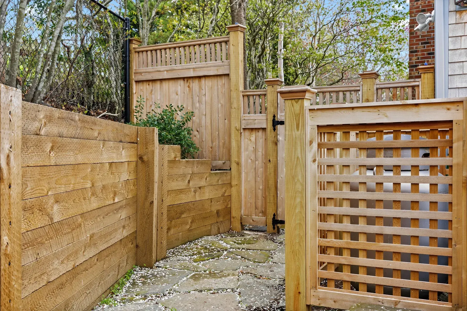 Wooden fenced patio with stone path and lattice screen, surrounded by trees