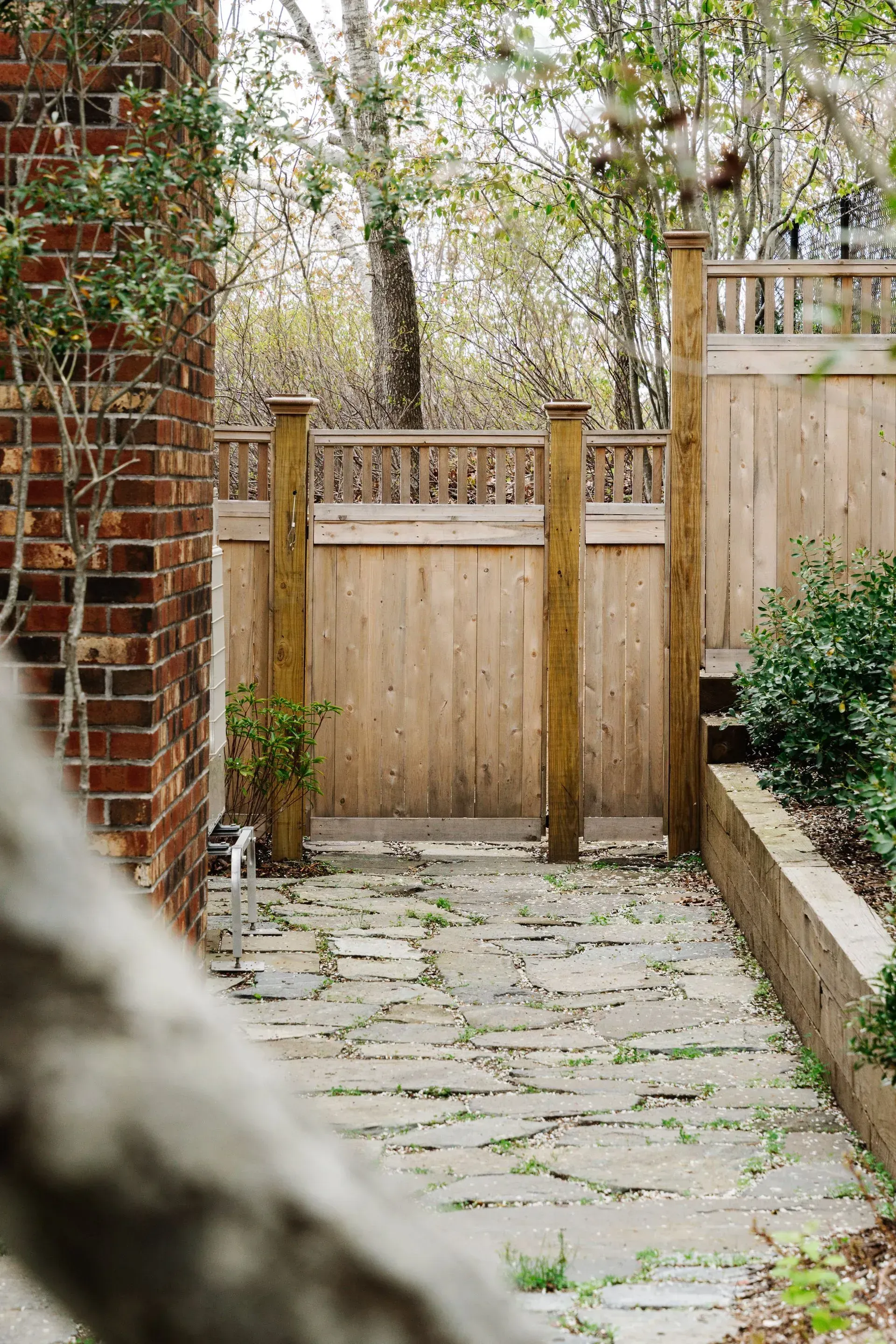 Stone path leading to a wooden gate in a small garden courtyard, with brick wall and trees beyond