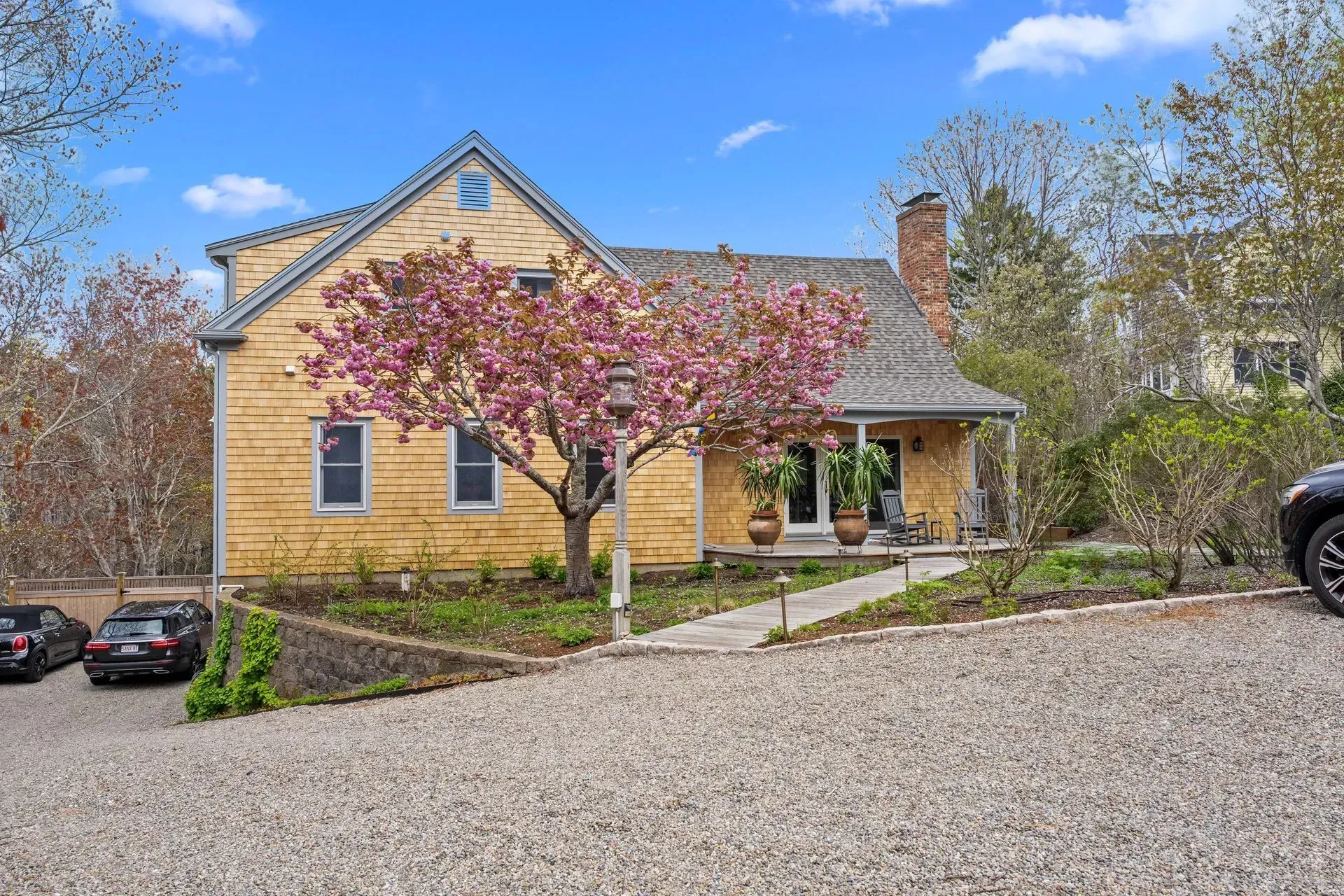 Yellow cottage with pink flowering tree, stone driveway, and blue sky